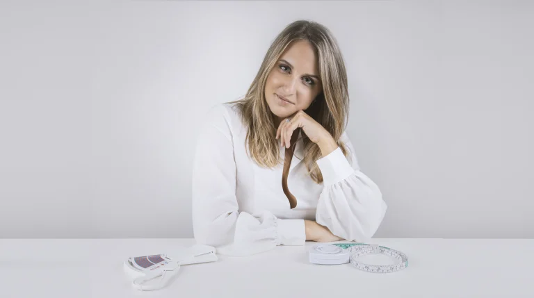 Alessandra Spadaro seduta alla scrivania con plicometro e metro da sarta